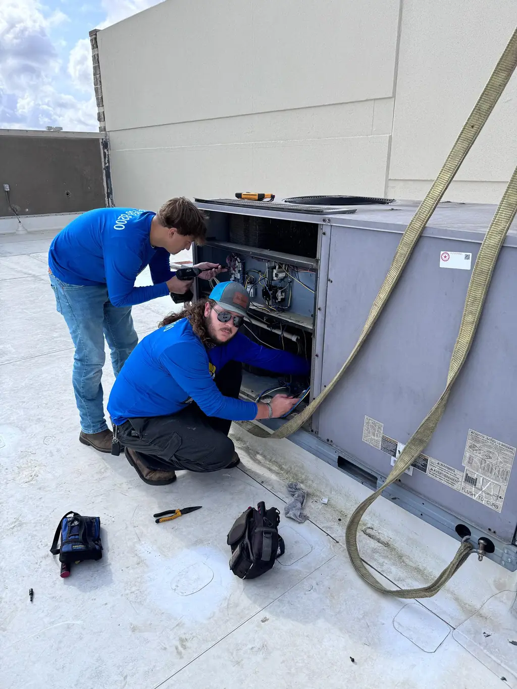 Two Air Monkey technicians working at the control panel of a rooftop unit in Tomball, Texas